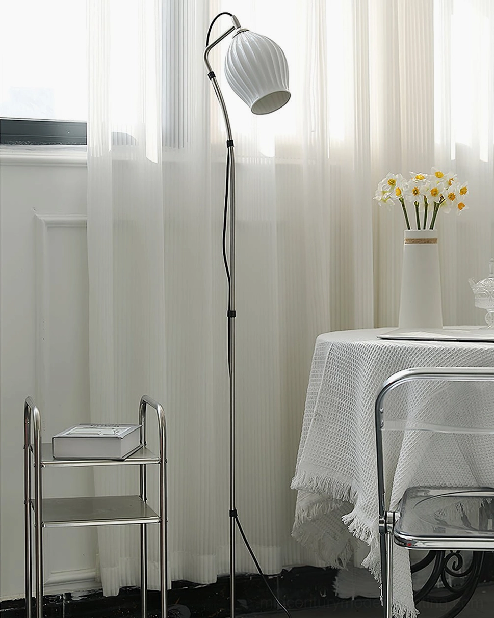 White ceramic ribbed arc floor lamp positioned in bright dining corner with black metal pole and sheer curtains