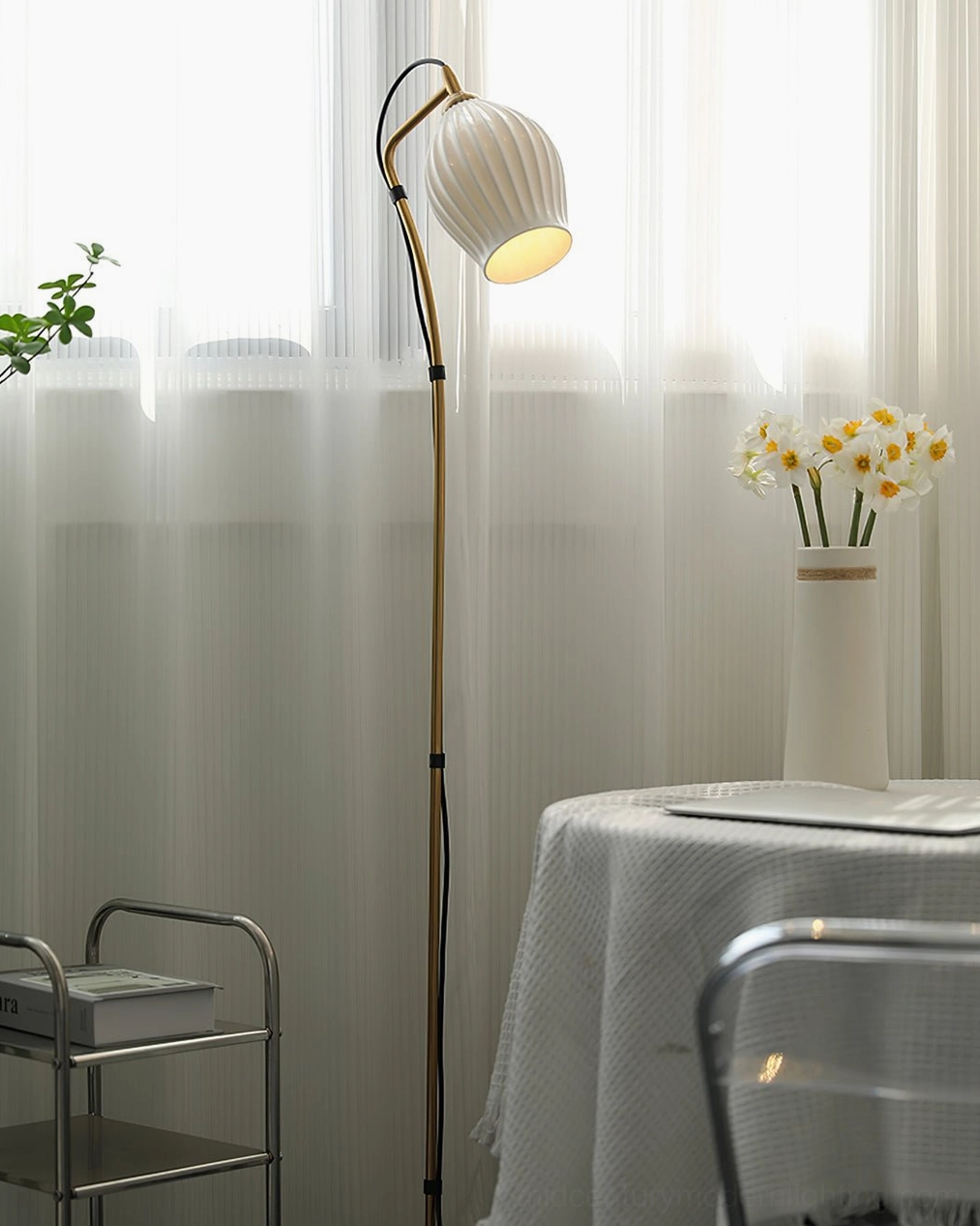 Gold metal curved arc floor lamp with white ceramic ribbed shade in low-angle close-up by window decor area