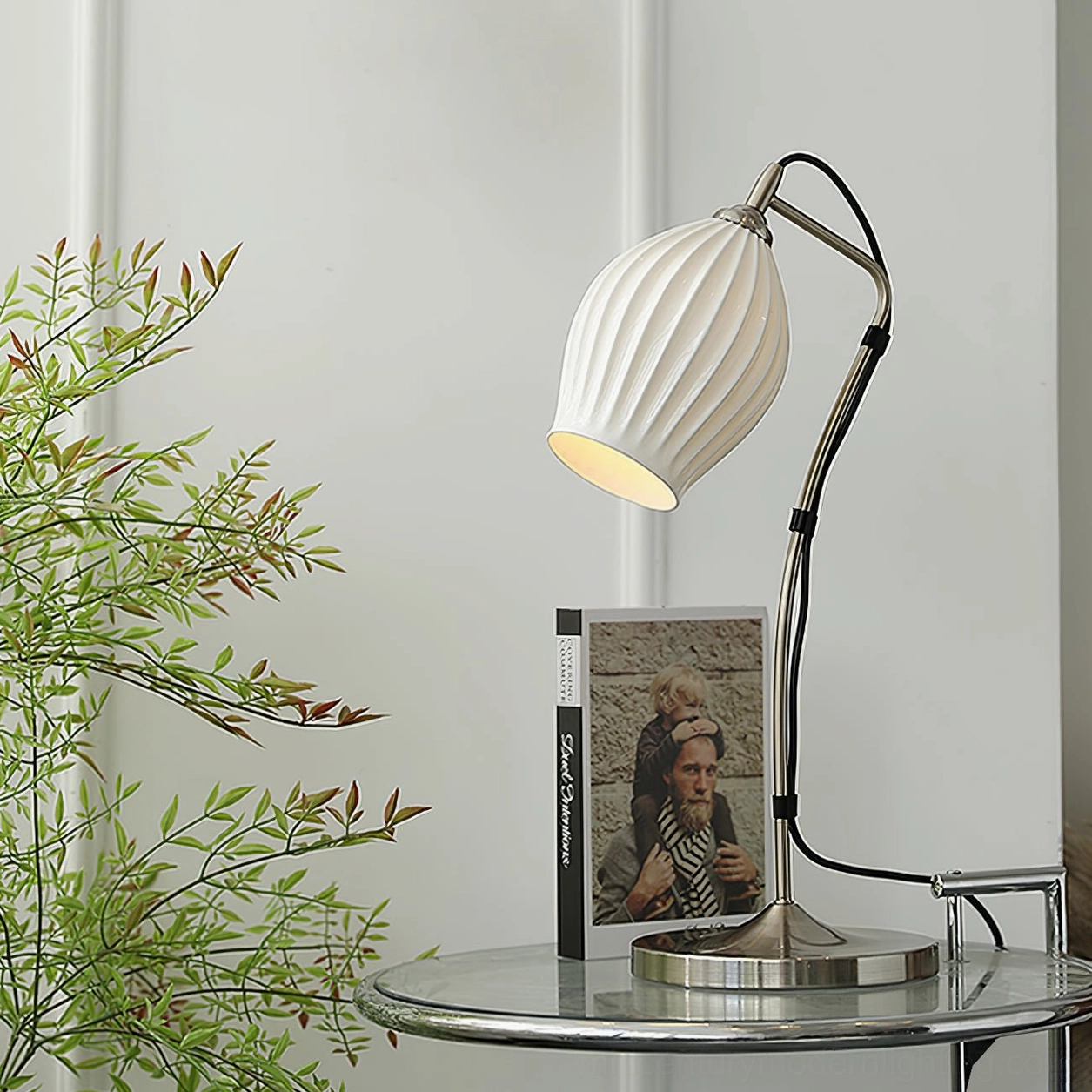 Ribbed ceramic table lamp in minimalist living room on side table paired with green foliage and photography book