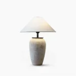 Sculptural ceramic table lamp with textured off-white base and conical fabric shade, front studio view