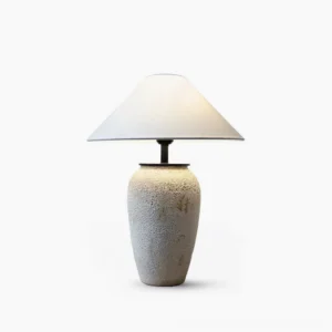 Sculptural ceramic table lamp with textured off-white base and conical fabric shade, front studio view