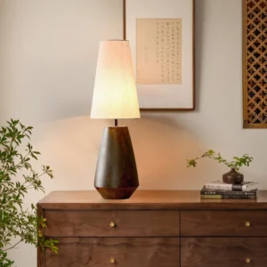 Ceramic tapered lamp placed on wooden dresser in living room with warm lighting, demonstrating interior design styling for mid-century modern spaces