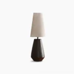 Ceramic tapered table lamp with rust-colored matte finish and beige fabric shade on white background, showcasing minimalist mid-century modern design