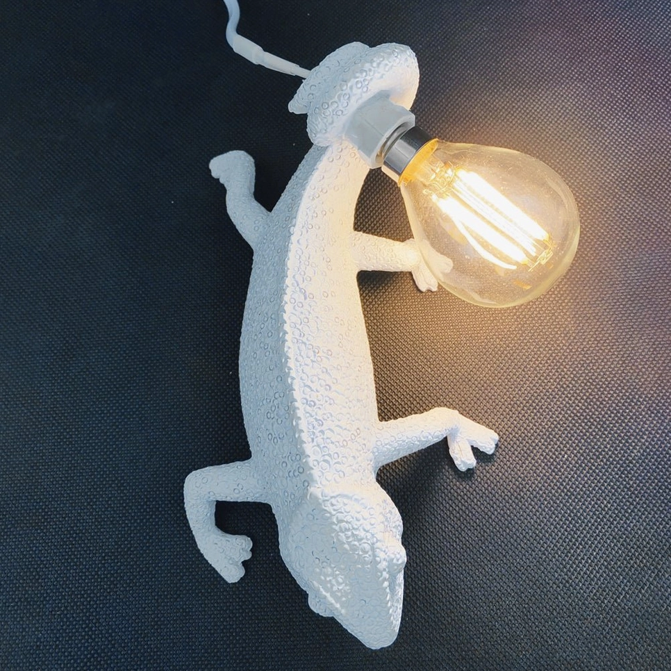 Chameleon wall lamp from side angle with white power cord visible, mounted on dark wall