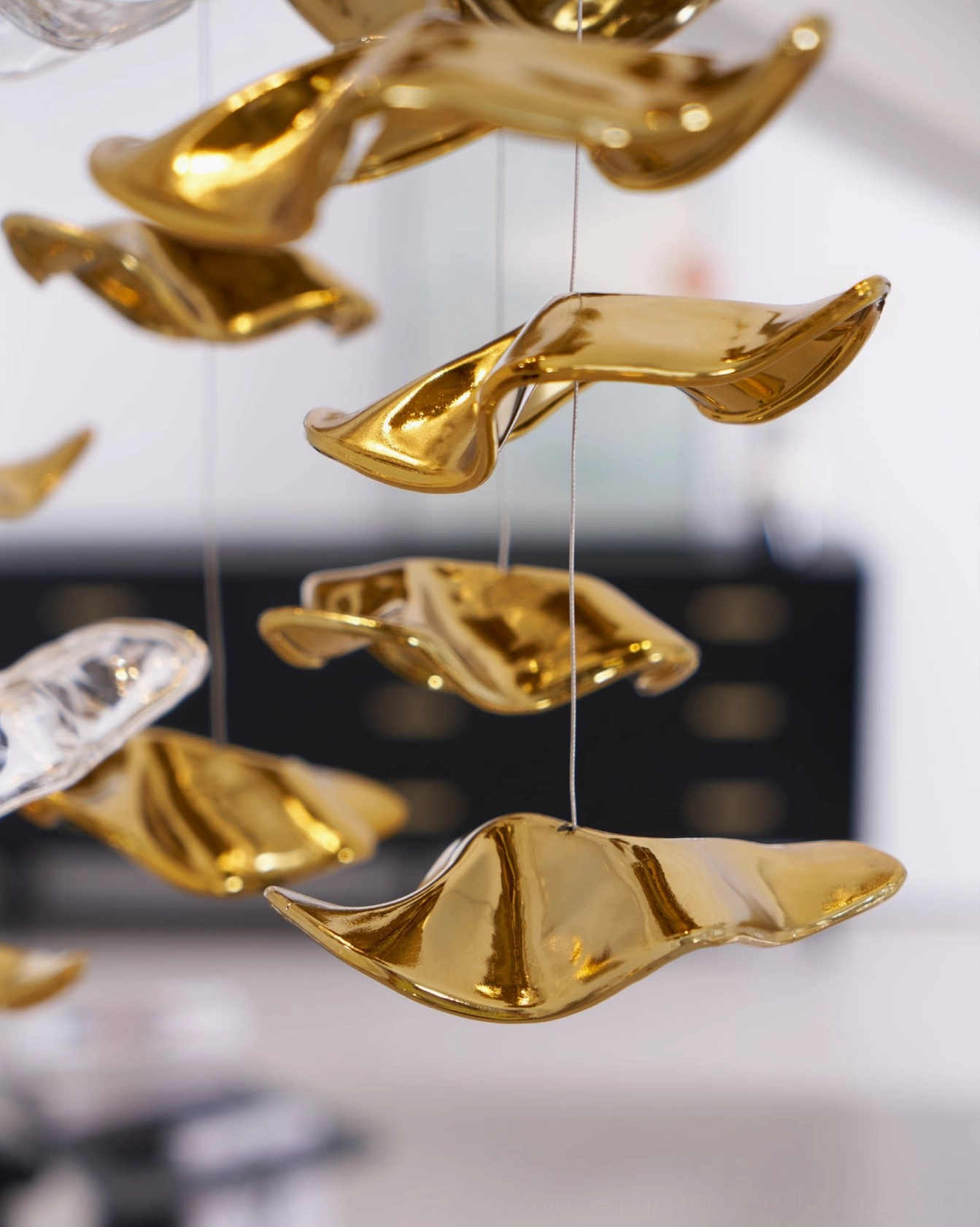 Close-up detail of polished golden wavy glass chandelier pendant with thin suspension wire macro view