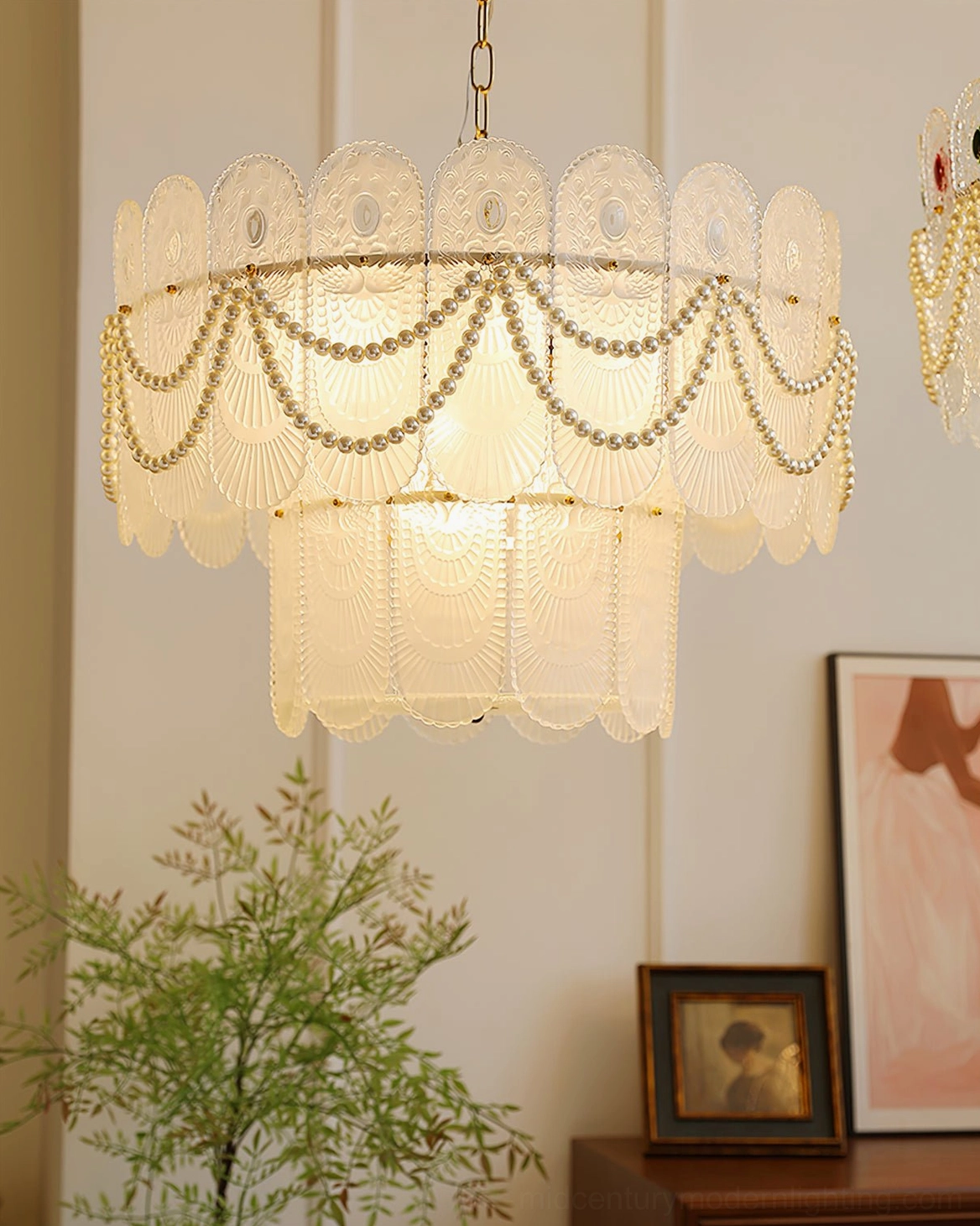 Scalloped glass chandelier illuminated in cozy living space with potted plant, framed wall art, and tabletop decor, front flat view with warm room lighting