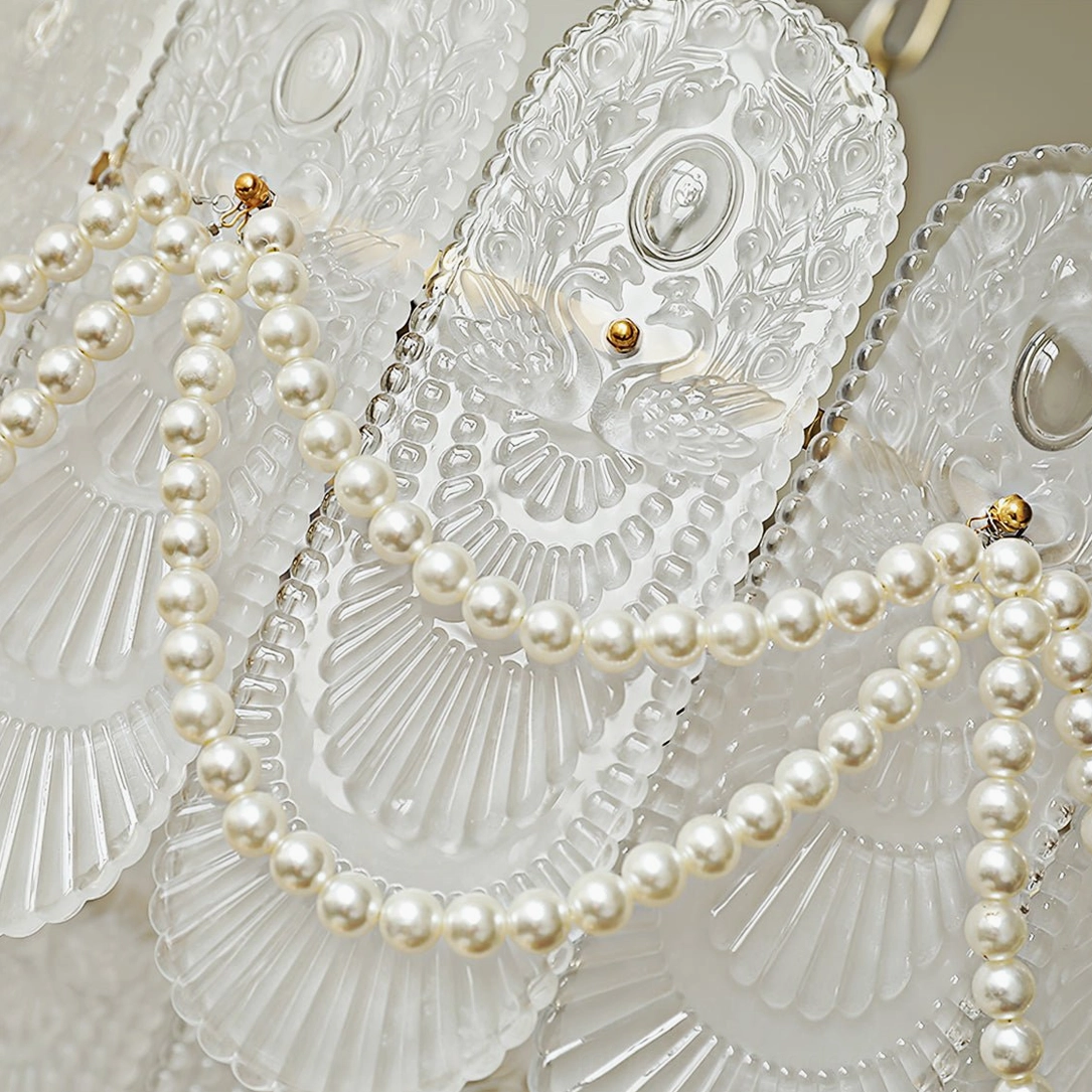 Close-up macro view of chandelier decorative metal trim, pearl bead swag draping, and engraved cameo glass detail on two-tier fixture