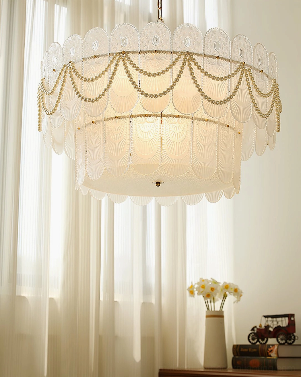Two-tier scalloped glass chandelier in sunlit interior room with sheer window drapes, matching desk decor visible, front overhead angle with natural daylight
