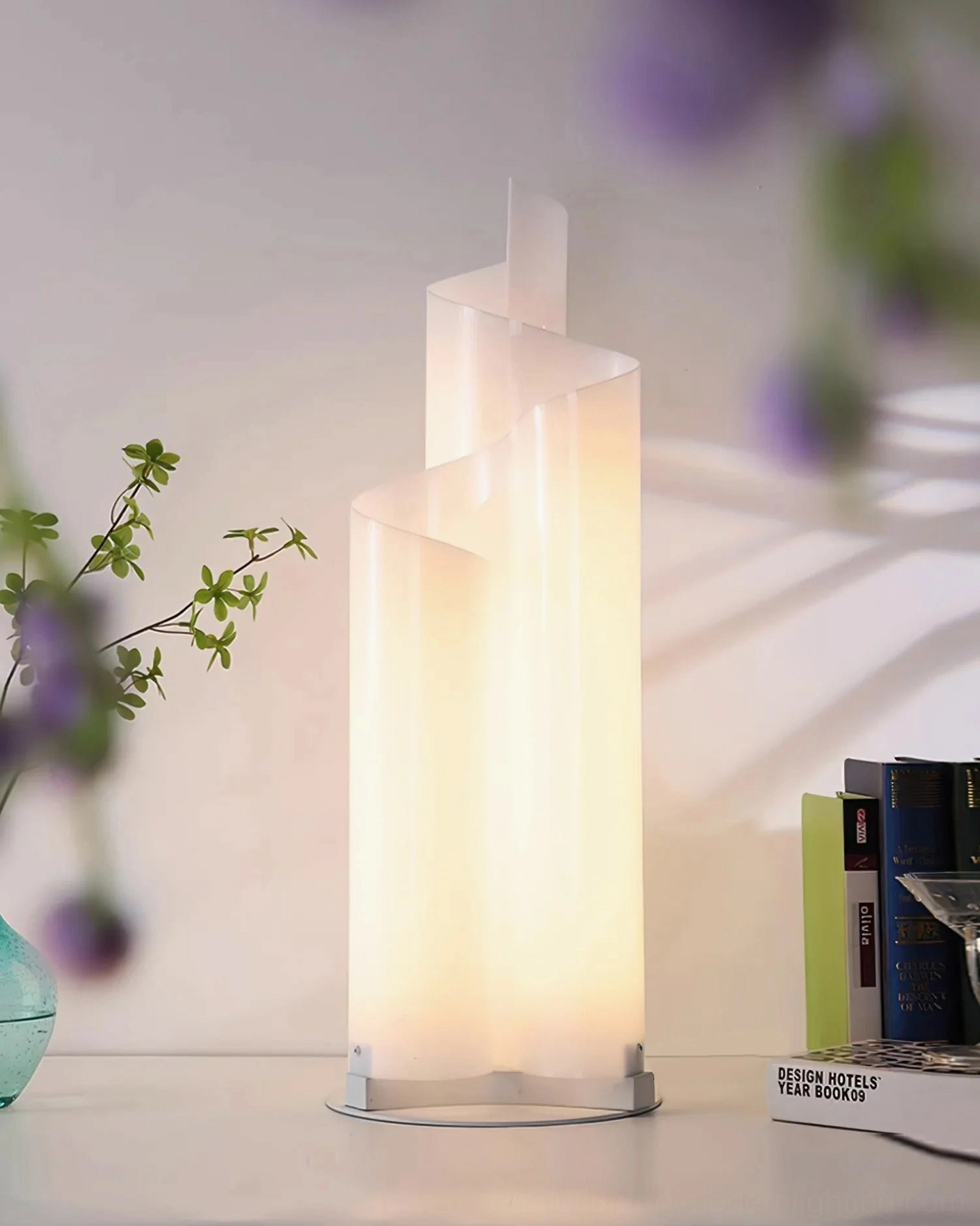 Chimera spiral table lamp three-quarter view showing layered twisted design stacked books and floral backdrop
