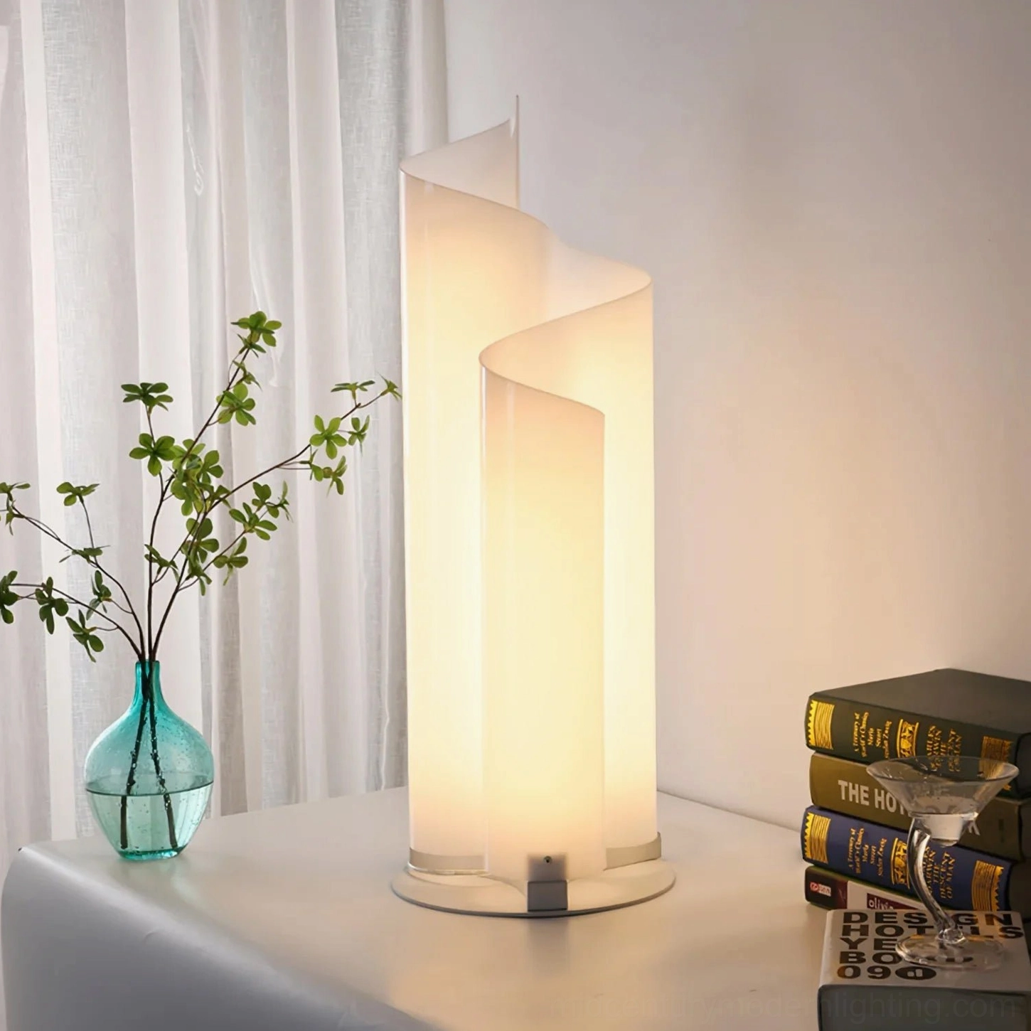 Illuminated chimera spiral lamp in living room beside sheer curtains creating warm ambient glow with books and blue glass vase