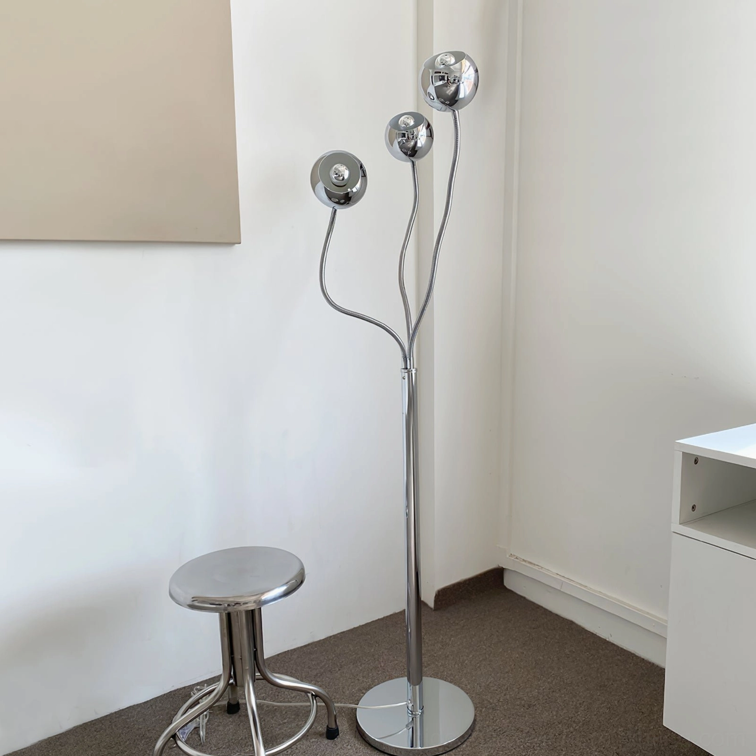 Silver chrome eyeball floor lamp with curved metal stems and round base paired with metal bar stool apartment corner