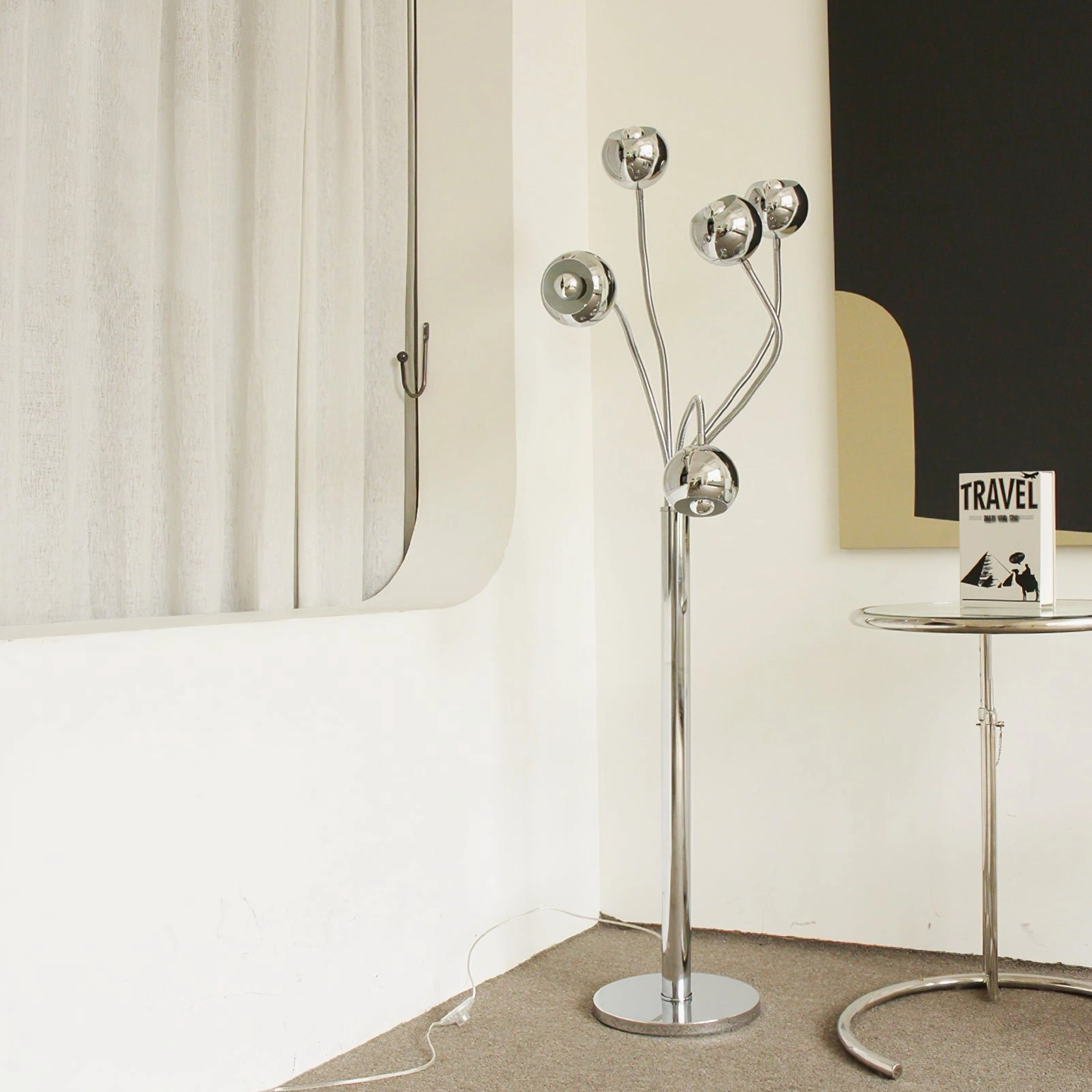 Chrome eyeball floor lamp styled in minimalist modern interior with round metal side table and neutral wall decor