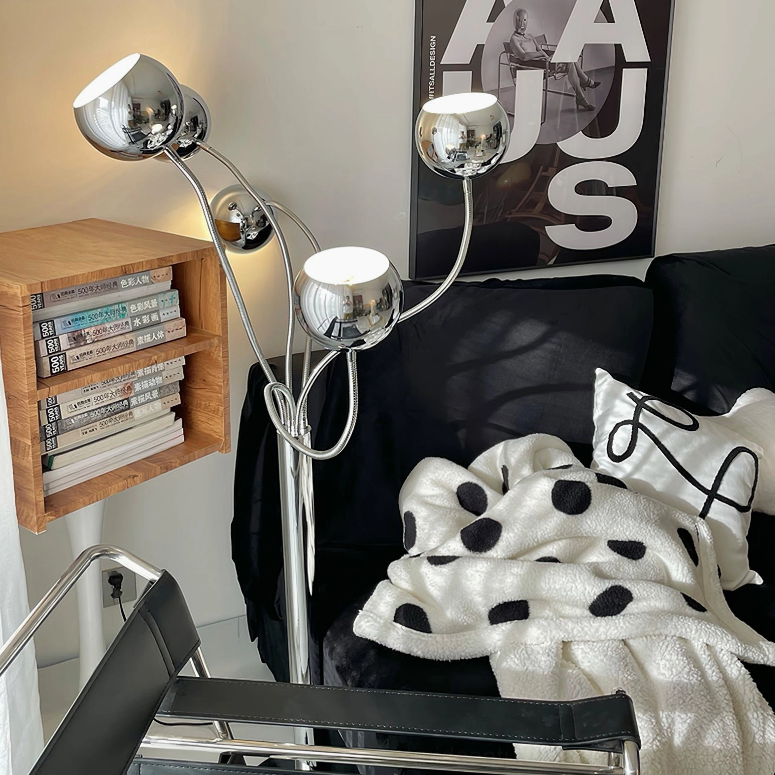Polished silver chrome eyeball floor lamp in cozy modern living room with black leather chair and geometric wall art