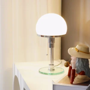 Chrome table lamp illuminated on bedroom nightstand with warm light, decorative figurine and sheer curtains creating cozy mid-century modern bedroom ambiance