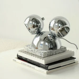 Polished chrome Mickey table lamp three-quarter elevated view on white side table with decorative books