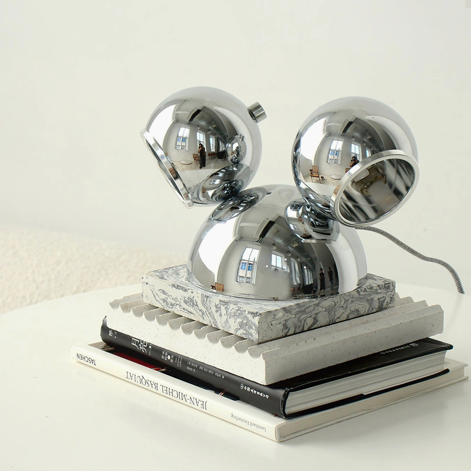 Polished chrome Mickey table lamp three-quarter elevated view on white side table with decorative books