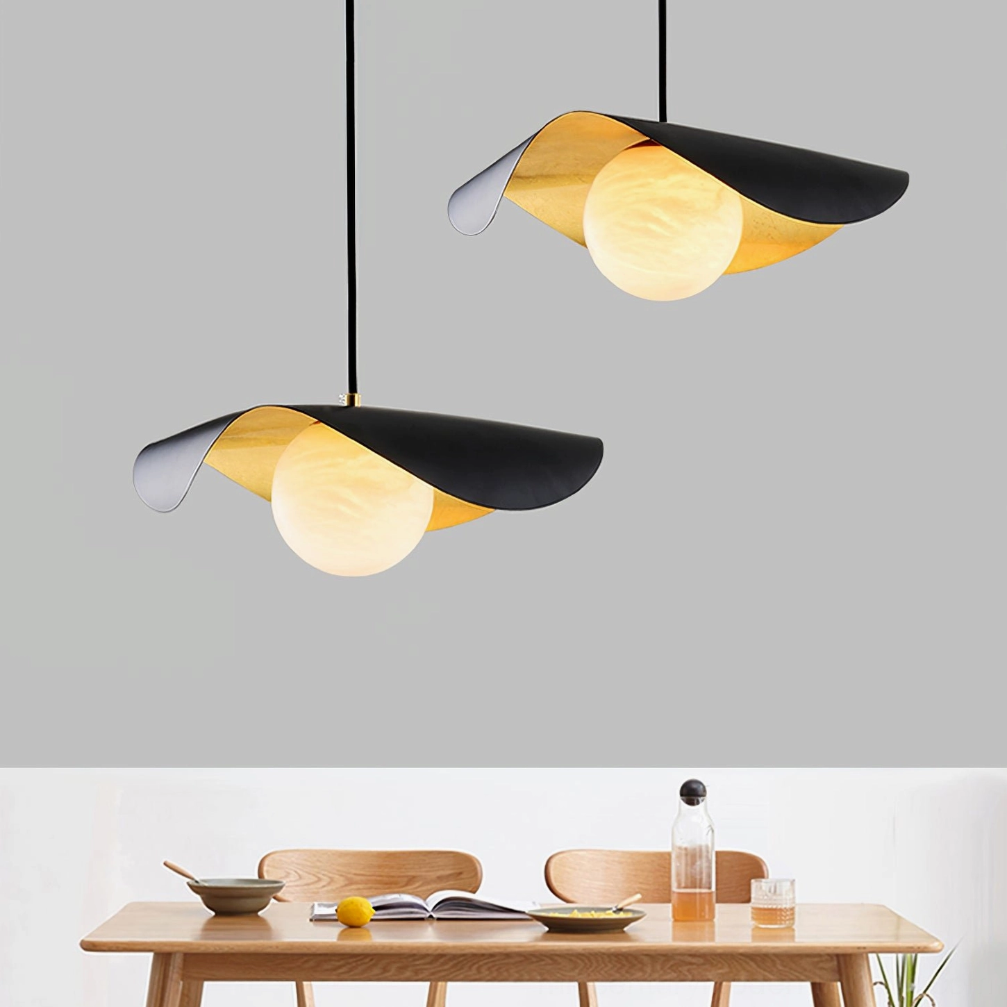 Two Cilla asymmetrical pendant lamps with matte black metal, gold inner shade, frosted glass globe bulb, product display and dining nook