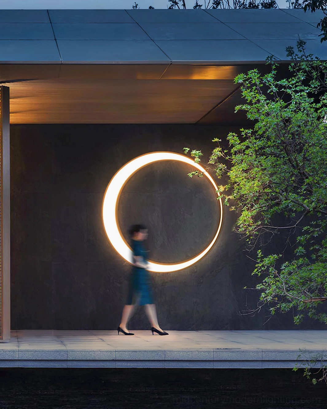 Warm glowing circular ring wall lamp on dark facade covered outdoor walkway dusk evening illumination side view