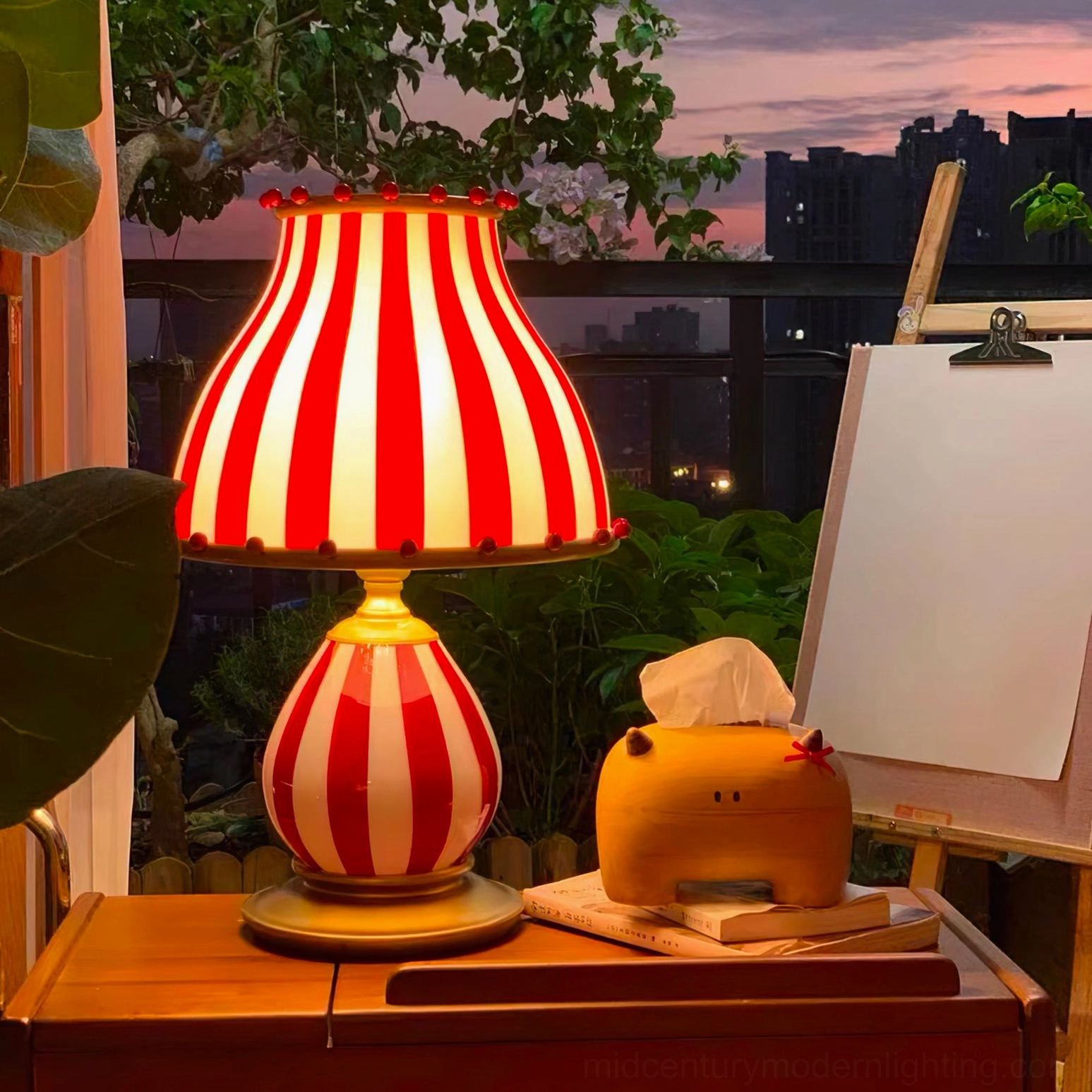 Carnival-themed striped table lamp on balcony at sunset with green plants and skyline