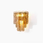Citrus wall sconce with tiered amber glass panels illuminated with warm light against white wall
