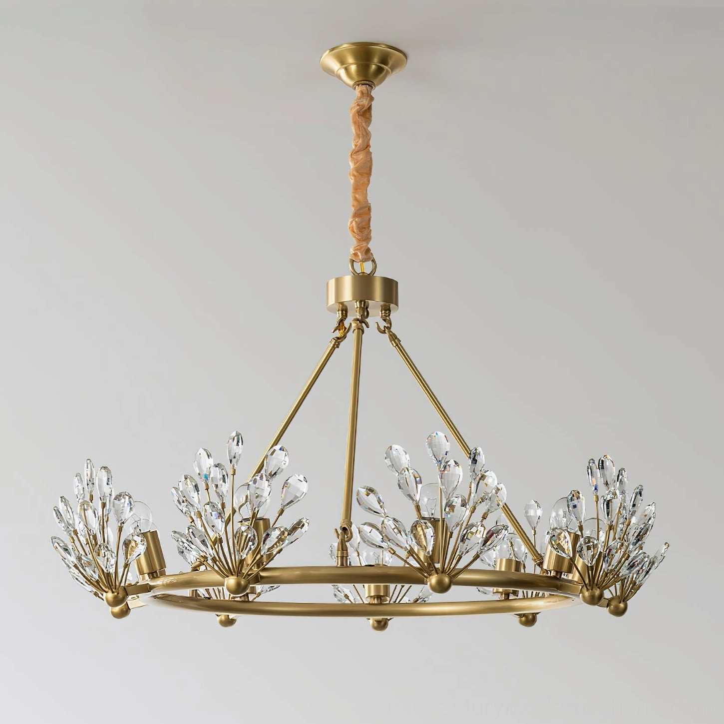 Clara Crystal Chandelier neoclassical design featuring clear crystal accents and warm brass finish against light gray indoor wall, front view demonstration