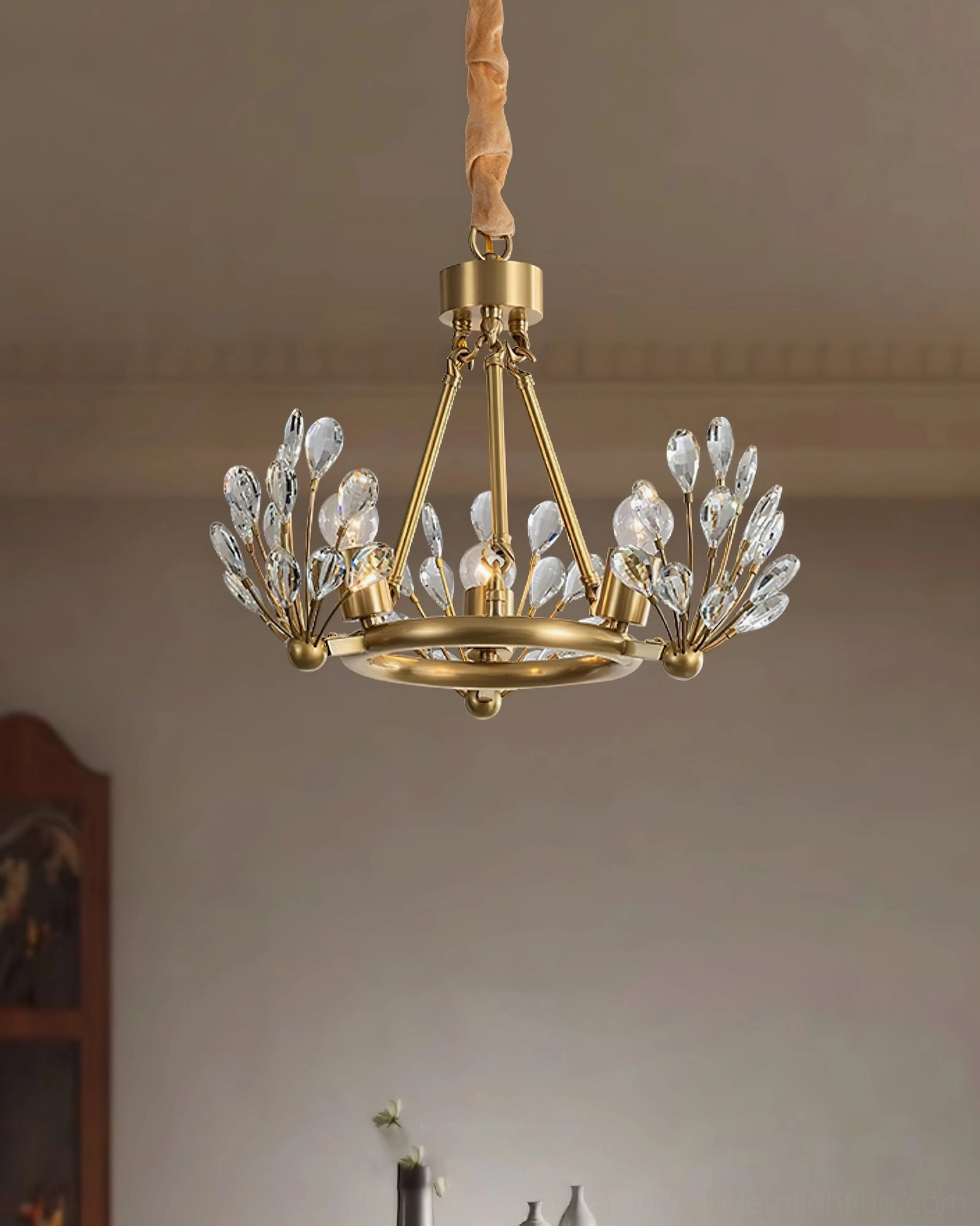 Small circular Clara Crystal Chandelier with brass frame and crystal decorations, overhead view against warm wooden furniture and home interior background