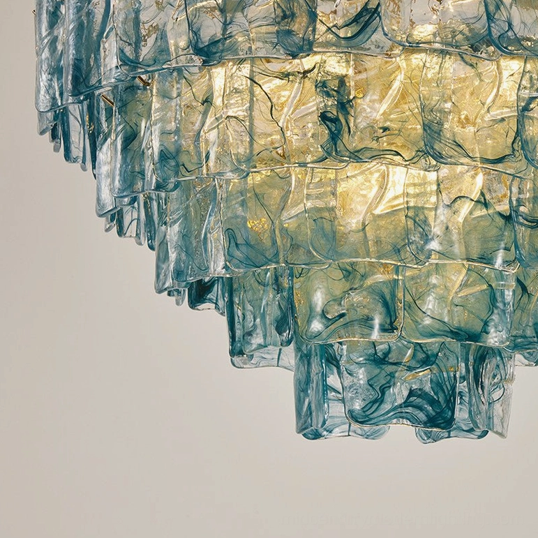 Side view of blue tiered glass chandelier with exposed brass hardware and internal light fixtures, low-angle studio photography