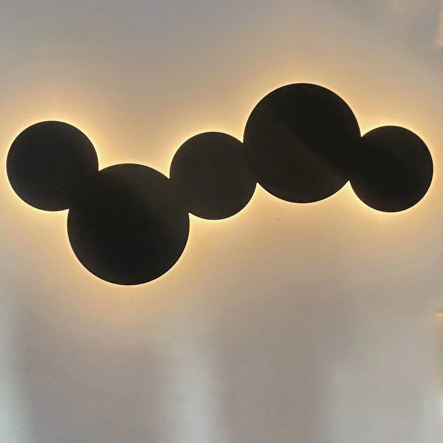 Close-up backlit matte black geometric disc wall sconce showing sculptural light diffusion and minimalist design detail