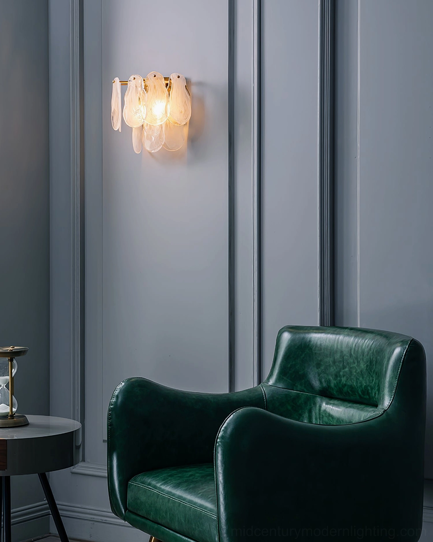 Cloud glass wall lamp mounted beside green leather sofa, side view showing warm atmospheric light on grey paneled wall