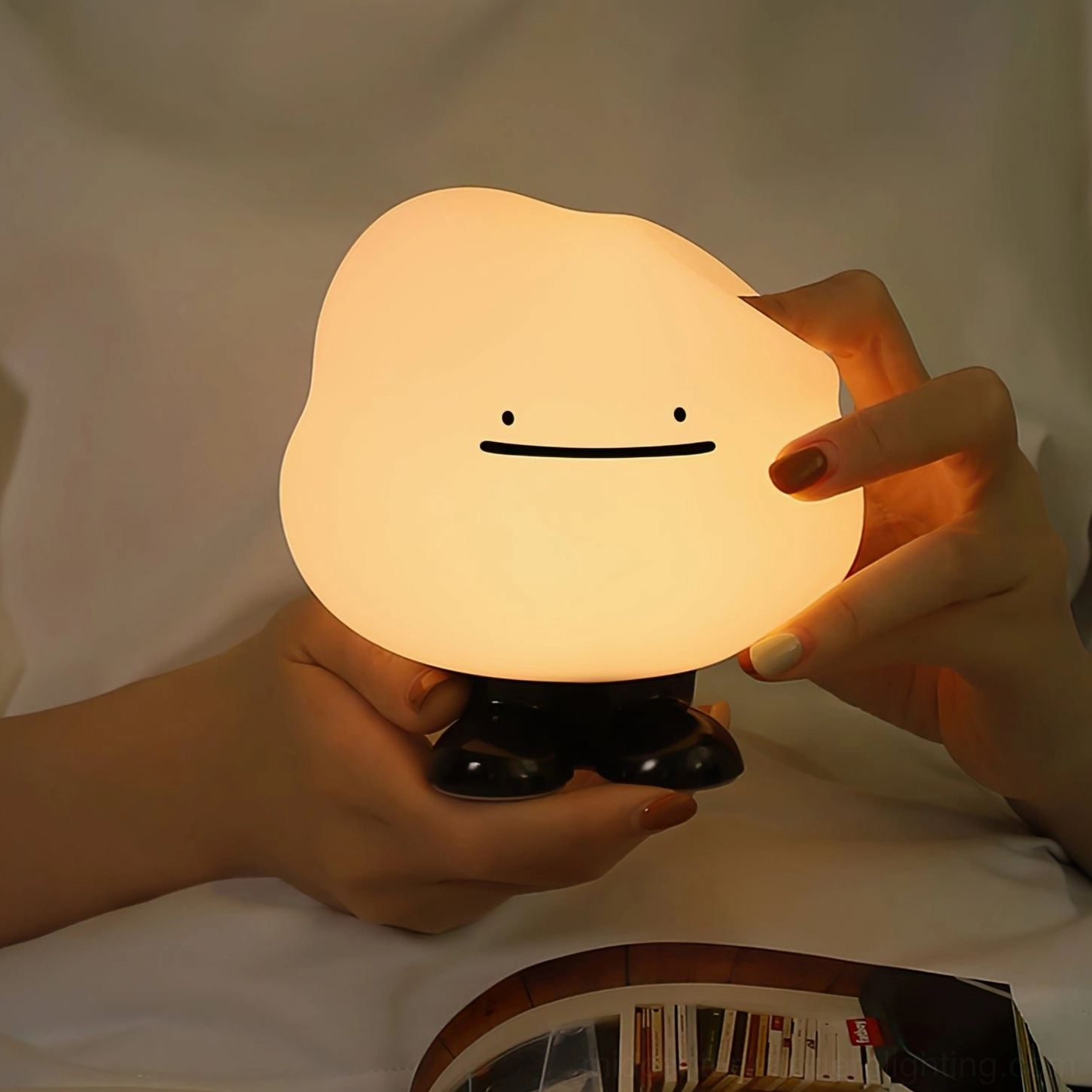 Close-up hands holding Cloud Night lamp showing soft warm amber glow and tactile silicone cloud design in bedroom setting