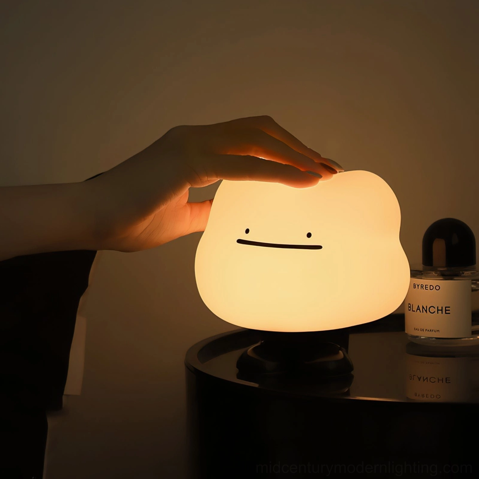 Hand activating touch control on Cloud Night lamp on bedroom nightstand with warm illumination and bedside perfume accessory
