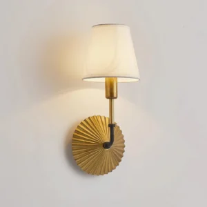 Close-up detail of Clove wall lamp pleated brass base with warm ambient light, showing texture and radiant metal finish, illuminated warm glow