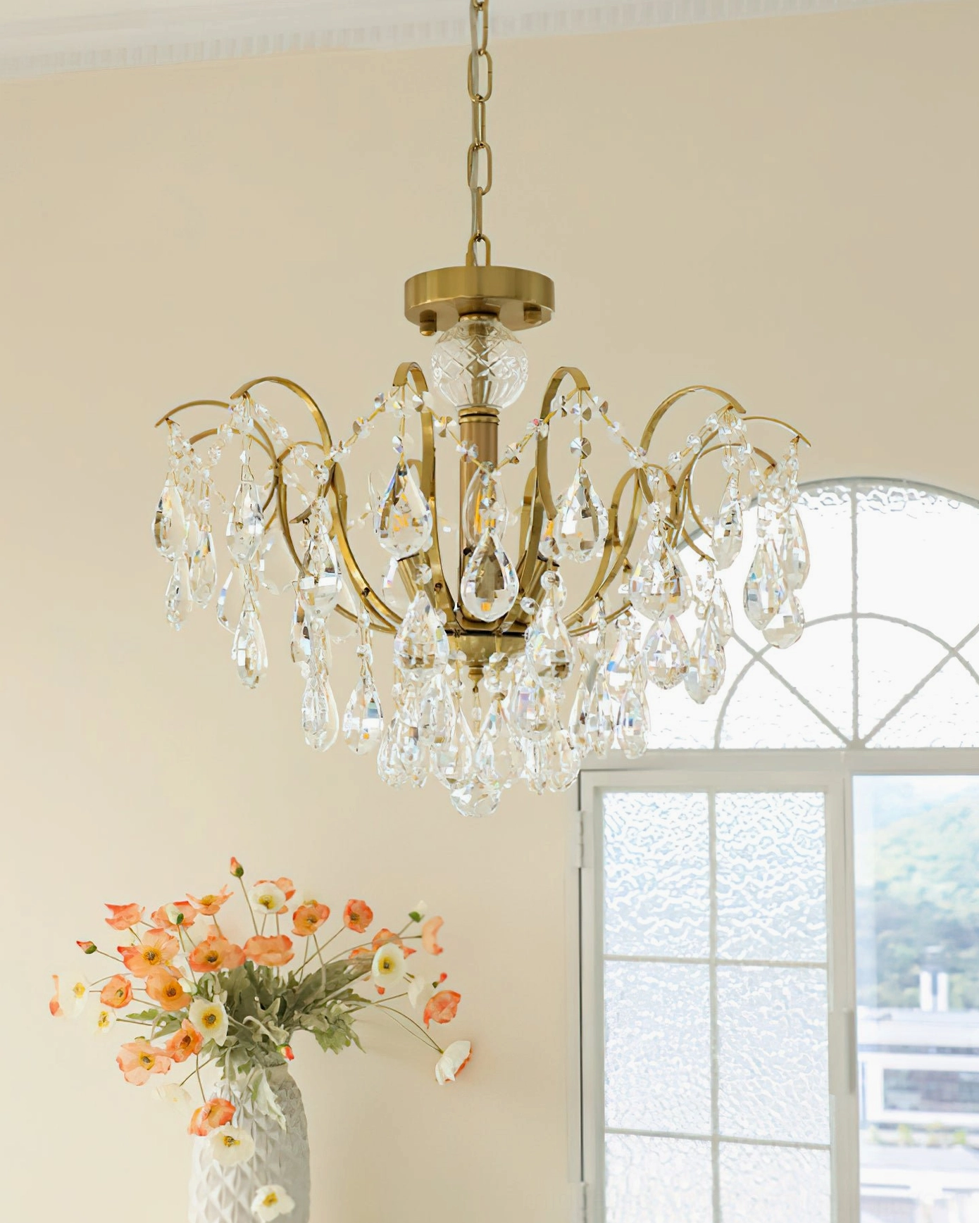 Side perspective of Colette Chandelier against minimalist wall with clear crystal ornaments and brass frame