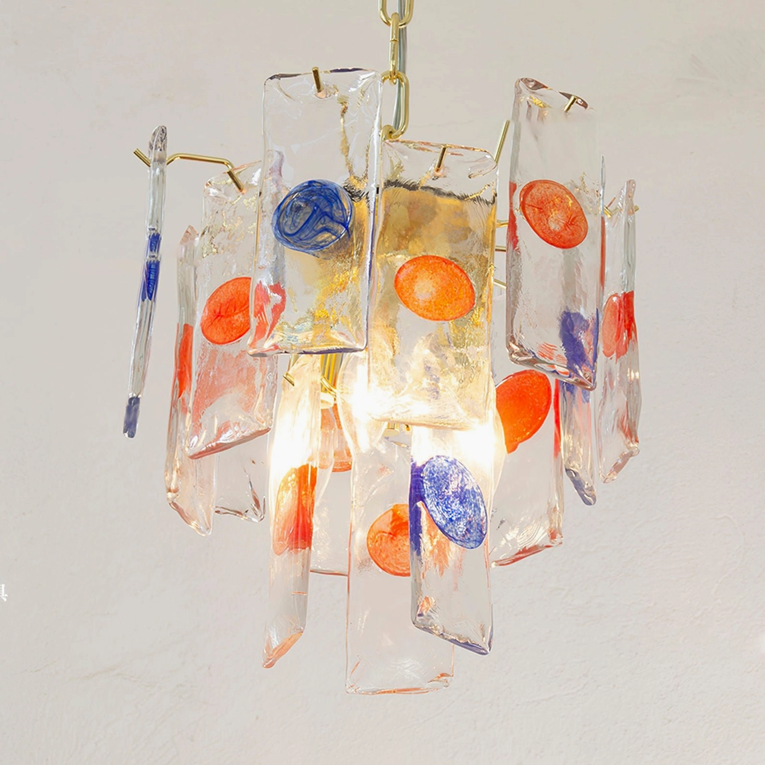 Low angle side view of mid-century pendant lamp with gold suspension chain, warm ambient glow through colored glass
