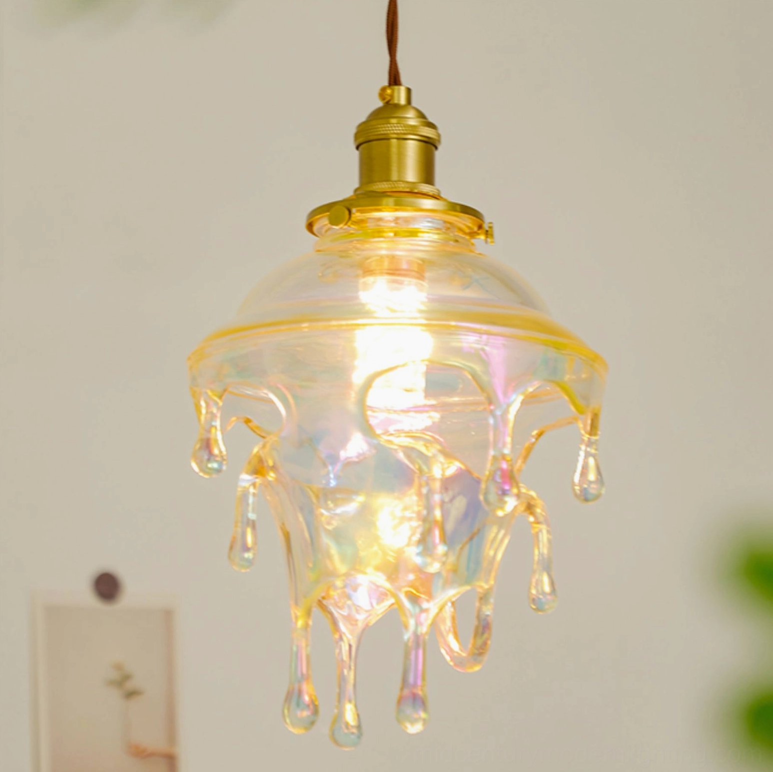 Colored glazed resin drip pendant with warm ambient light illuminating iridescent glass and brass hardware