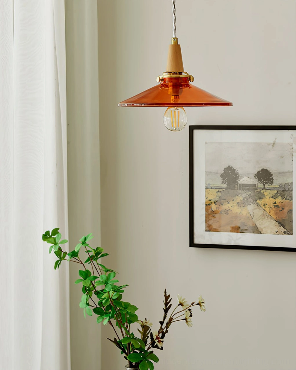 Small amber glass pendant shade in interior corner with green potted plant below and framed landscape artwork