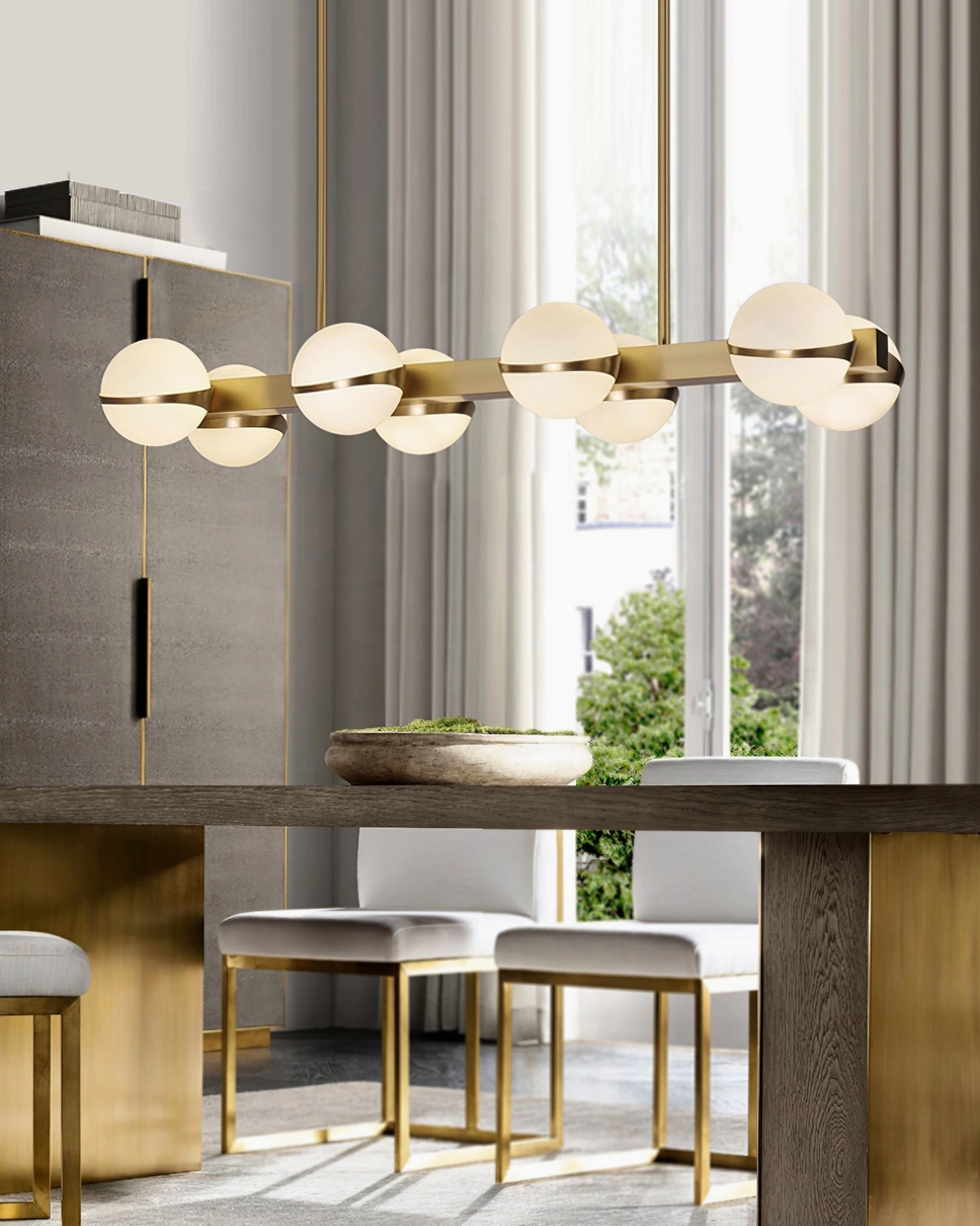 Small circular brass pendant chandelier in modern kitchen dining space with pink accent wall, compact luxury design