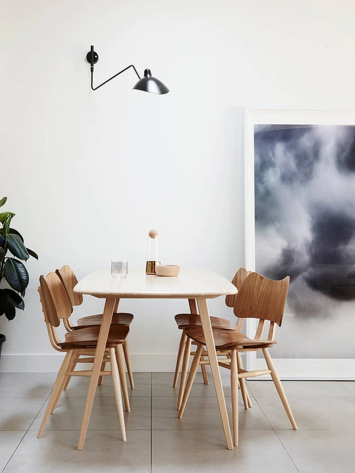 Compact single-arm spider sconce in matte black mounted above minimal dining area table