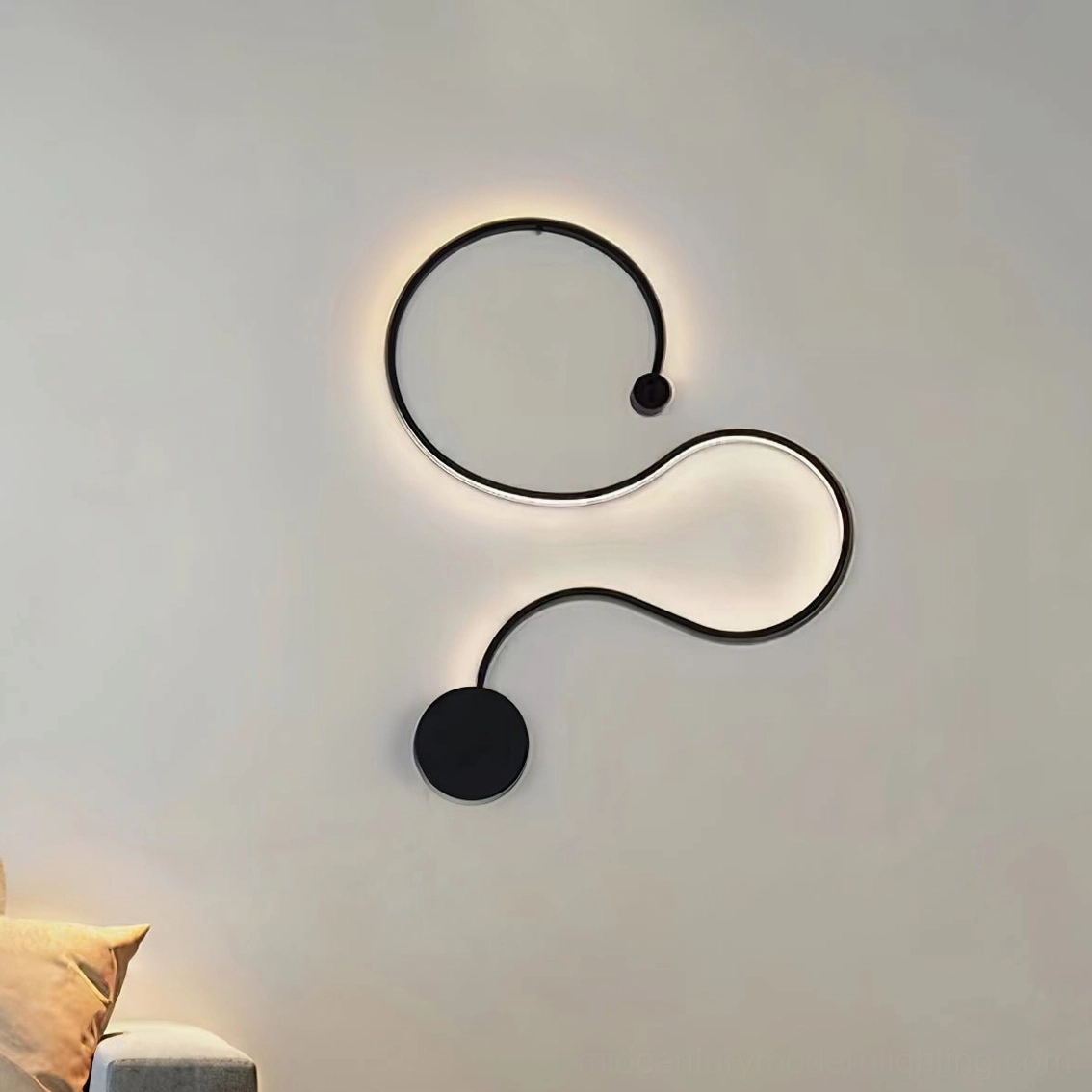 Compact curved snake wall sconce accent lighting on bedroom wall in matte black finish