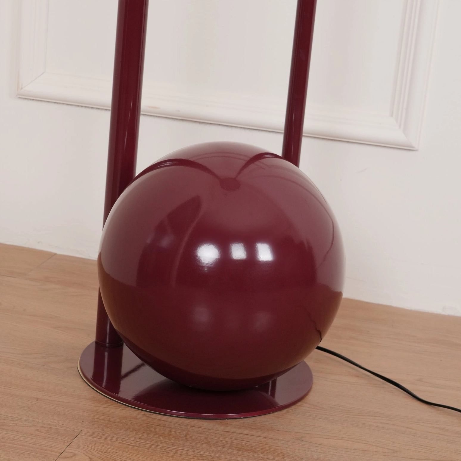 Close-up detail of composition floor lamp base - glossy burgundy metal spherical form with cylindrical support poles on wood floor