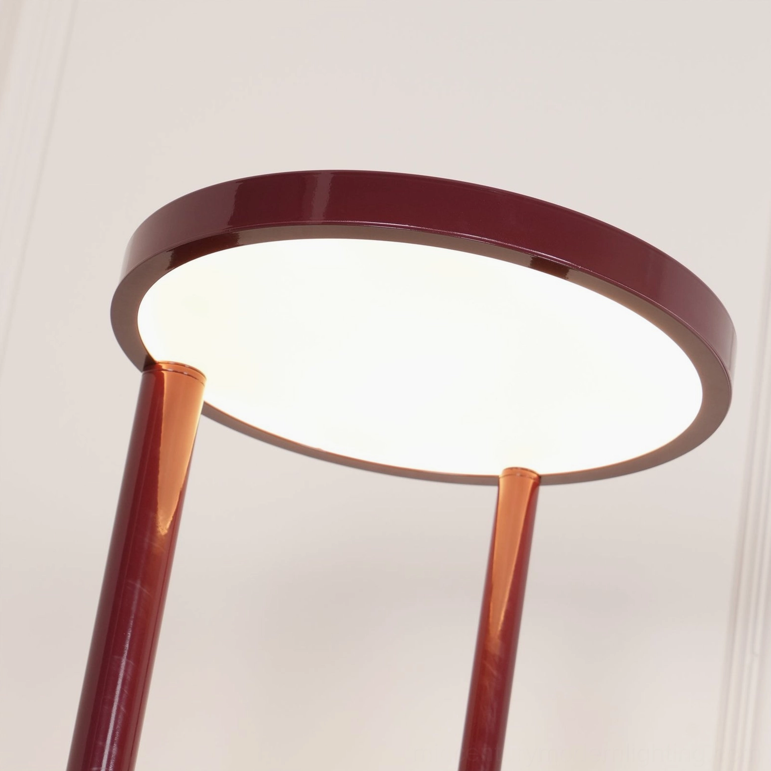 Composition floor lamp head illuminated - lit circular acrylic diffuser with burgundy metal frame casting warm light on white background