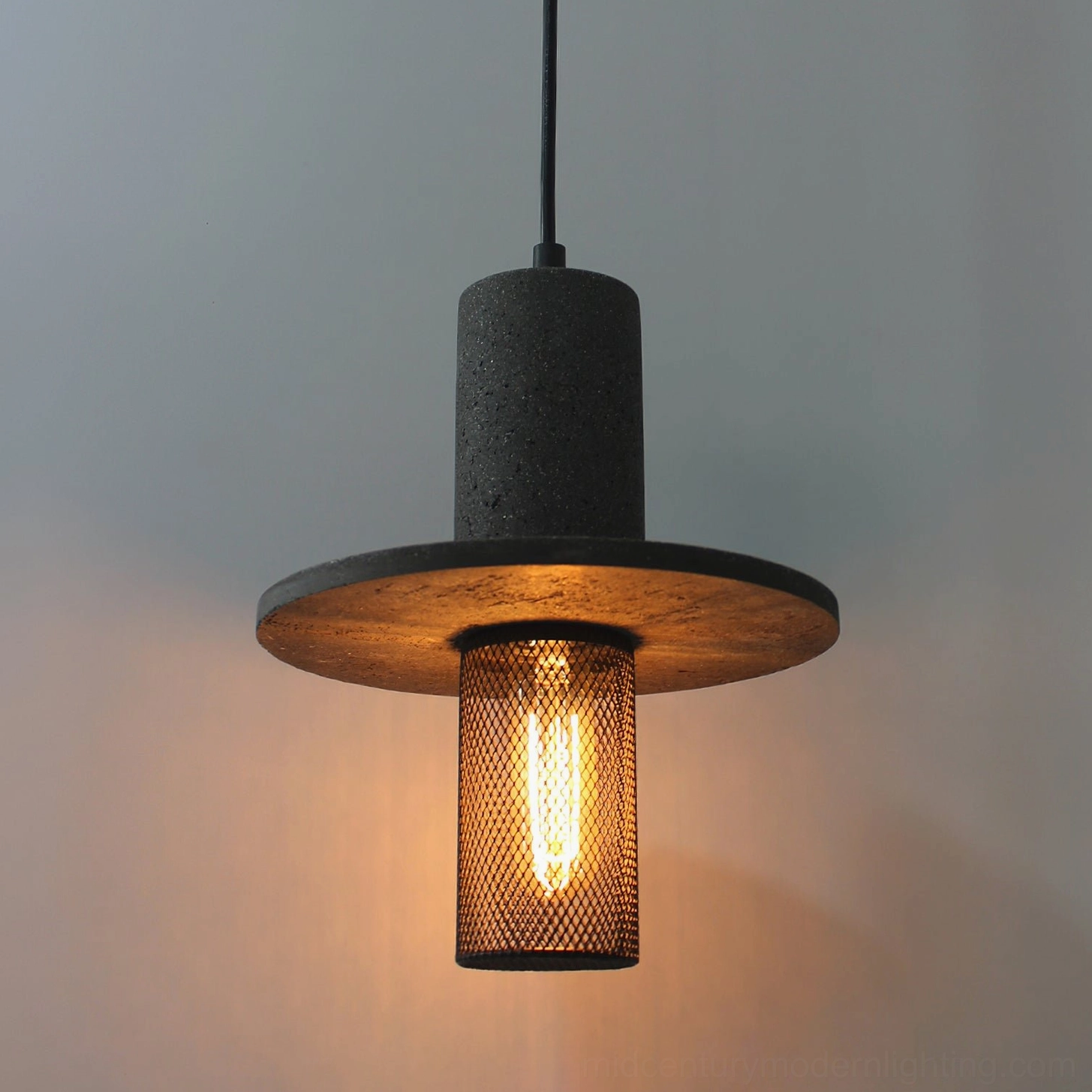 Close-up detail of Condo pendant light showing warm glowing Edison filament bulb through black diamond mesh diffuser and textured travertine finish
