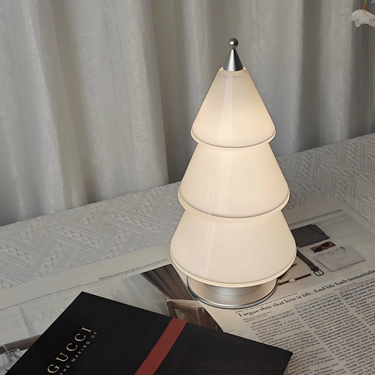 Contemporary minimalist cone-shaped table lamp with milk white acrylic shade and metal base on linen table surface