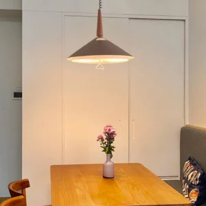 Cone pendant light installed above wooden dining table in warm minimalist home setting