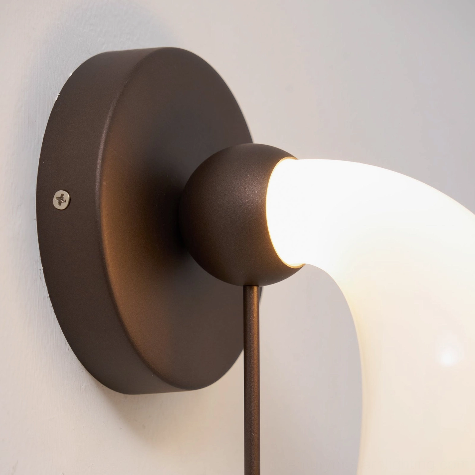Contemporary bent glass wall sconce showing warm white LED glow and shadow patterns created by sculptural metal design
