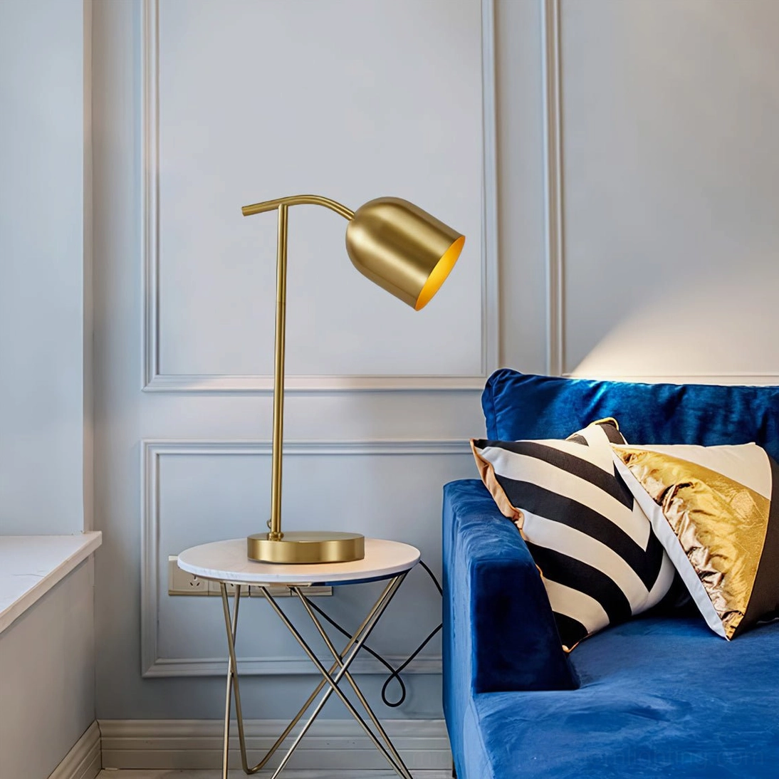 Brass gooseneck table lamp on round metal side table next to blue velvet sofa in contemporary living room