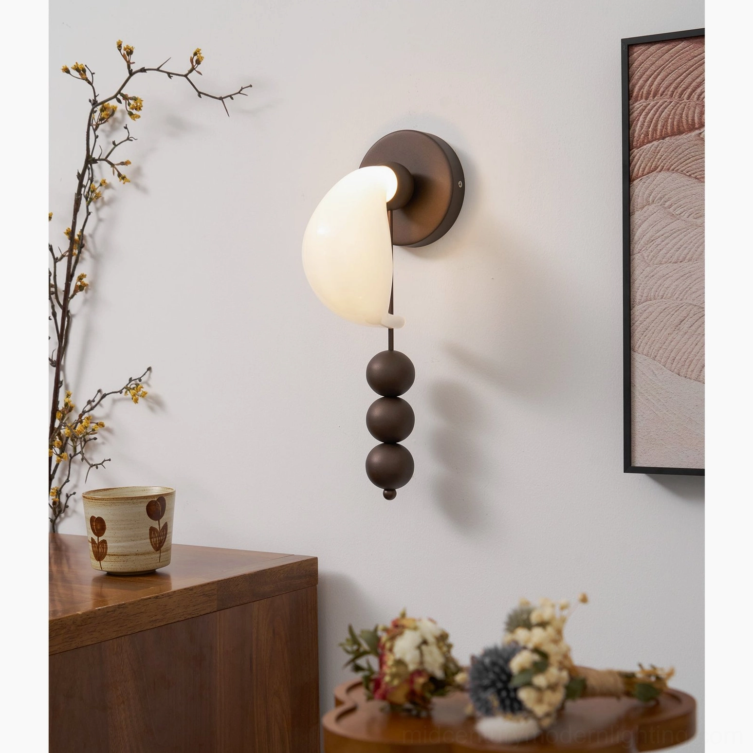 Contemporary glass wall sconce with semi-transparent milky white shade and bronze metal base, oblique view with floral home decor