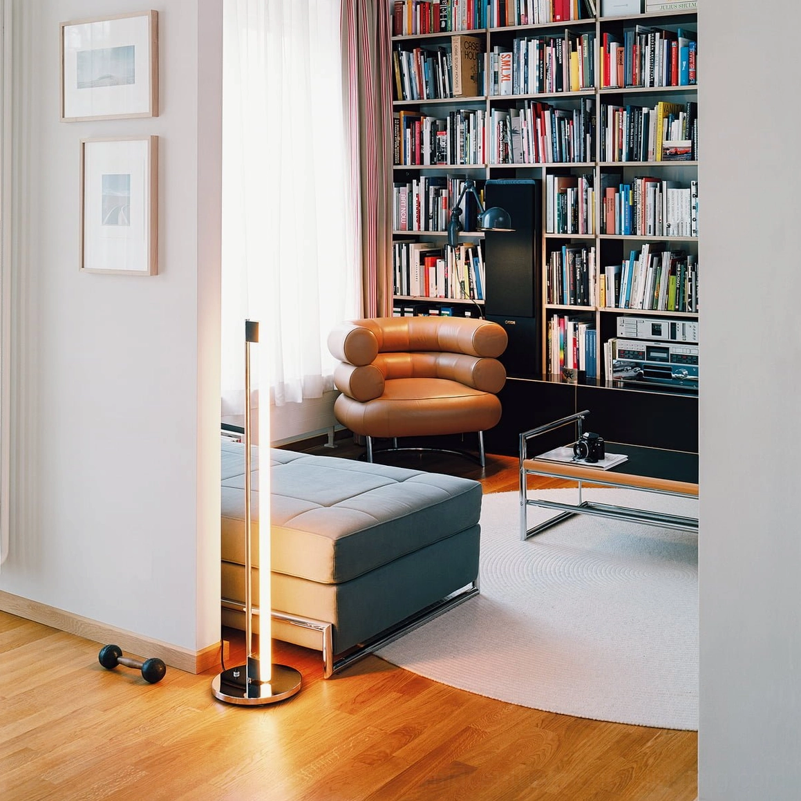 Tube floor lamp in home library with leather lounge chair providing warm ambient light for reading