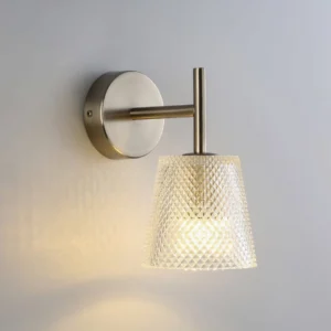 Contemporary glass wall sconce with faceted trapezoid shade mounted on gray wall, ambient lighting fixture