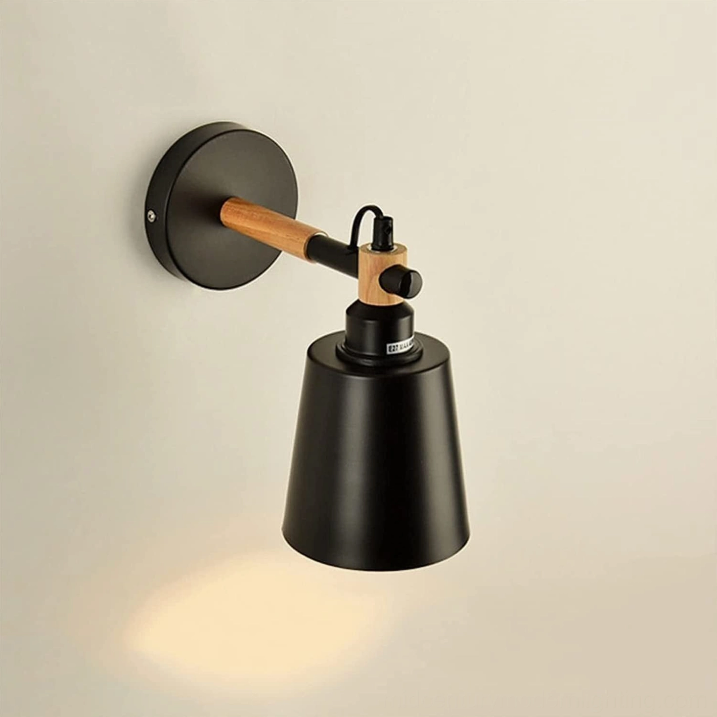 Black Copita wall lamp with adjustable metal arm and wood accent detail on neutral wall backdrop